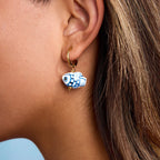 Close-up of an ear wearing a gold hoop earring with a blue and white fish charm.