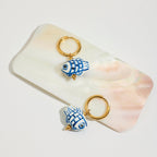 Two blue and white fish-shaped keychains on a shell with a white background