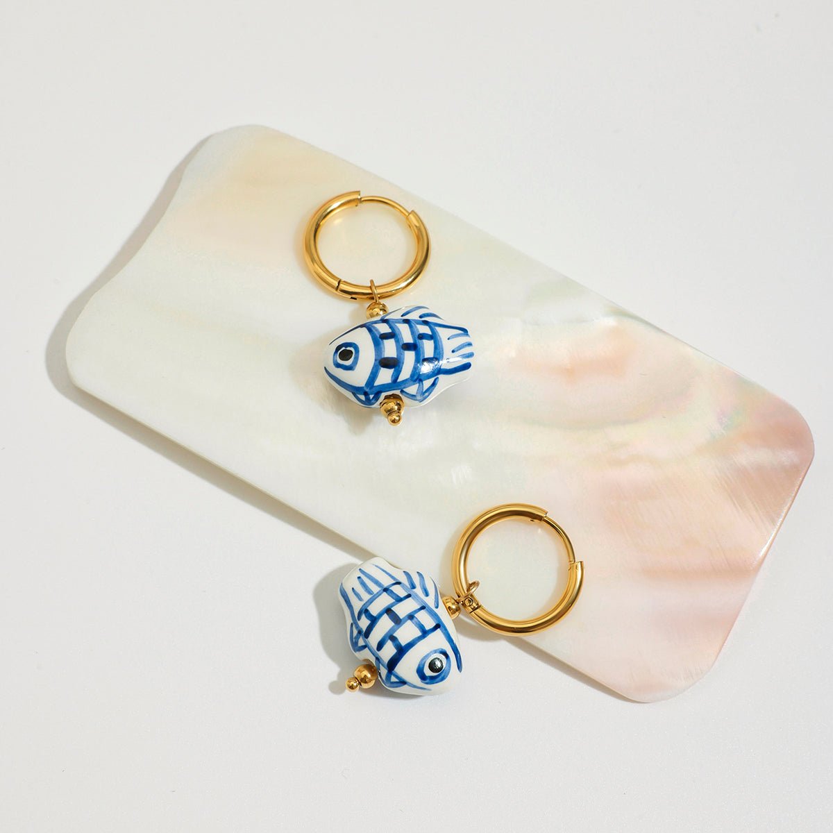 Two blue and white fish-shaped keychains on a shell with a white background