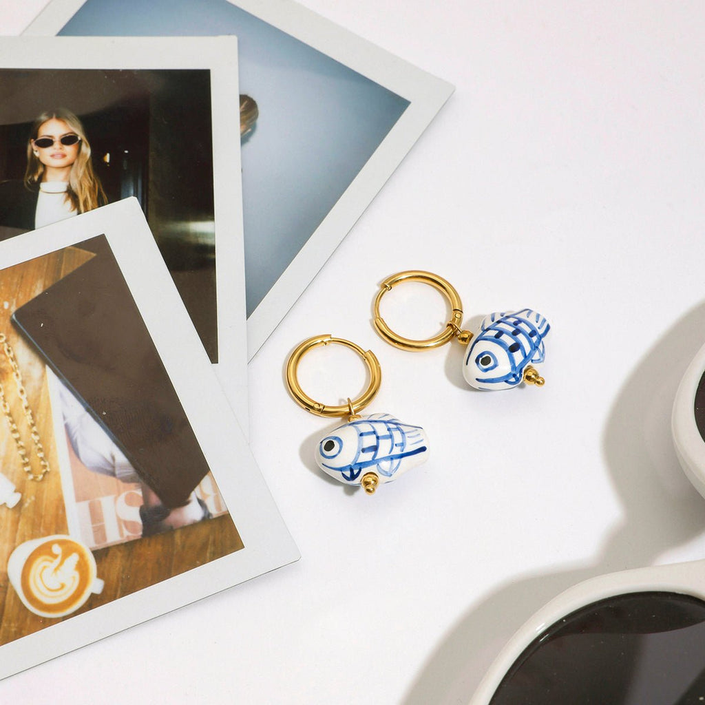 Two keychains with fish designs on a white surface with photos and sunglasses.