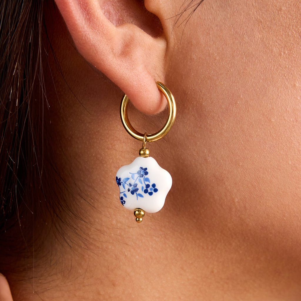 Gold hoop earring with a white floral pendant worn by a person.