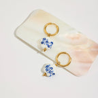 Pair of gold hoop earrings with floral charms on a marble surface