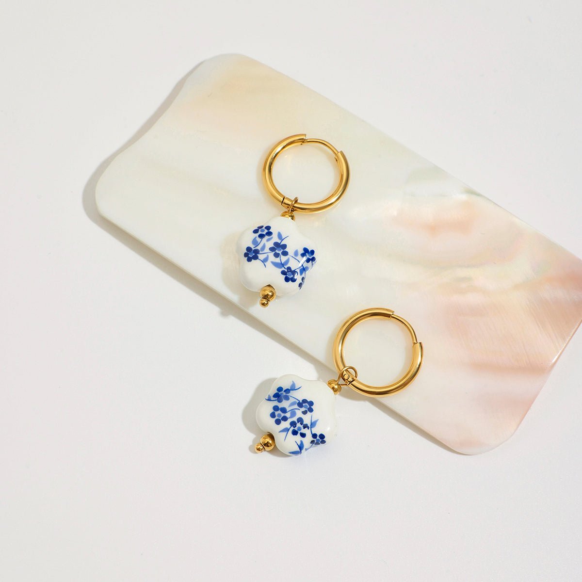 Pair of gold hoop earrings with floral charms on a marble surface
