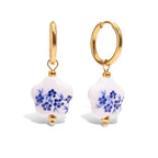 Gold hoop earrings with white and blue floral designs on a white background
