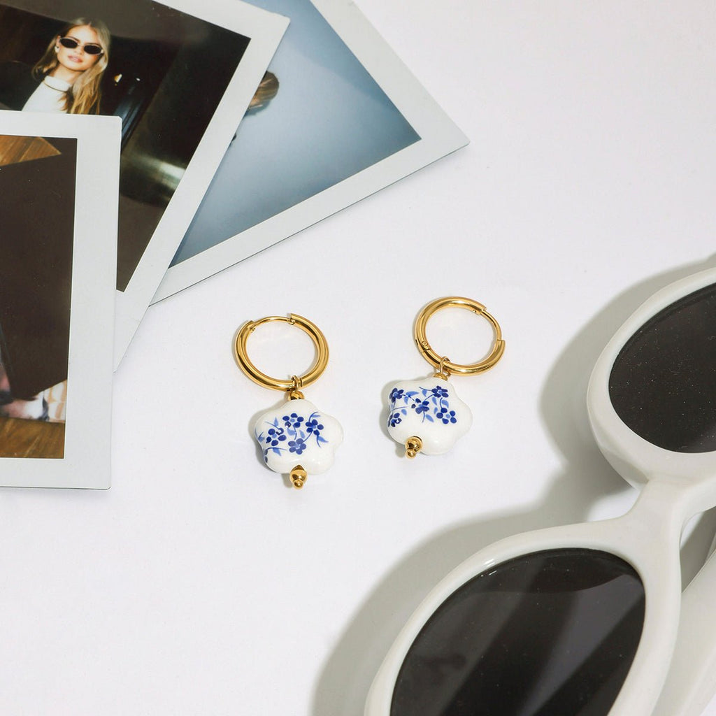 Pair of earrings with floral design on a white surface with sunglasses and photo frames.