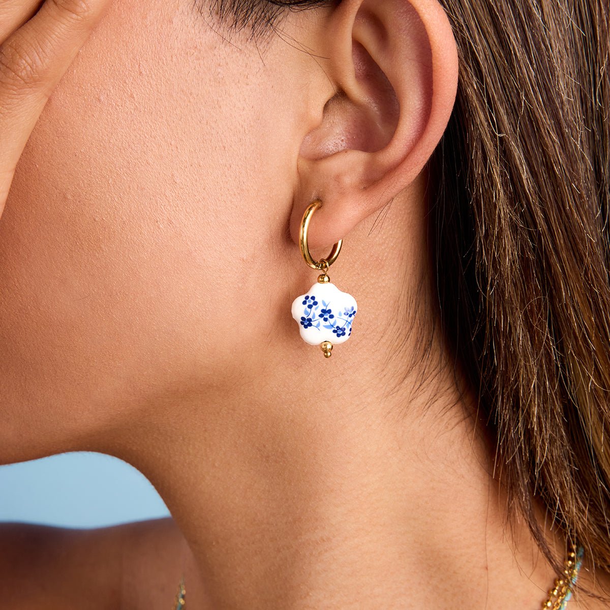 Close-up of an ear wearing a gold hoop earring with a floral bead.