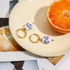 Pair of earrings with blue floral design on a white plate with an orange half.