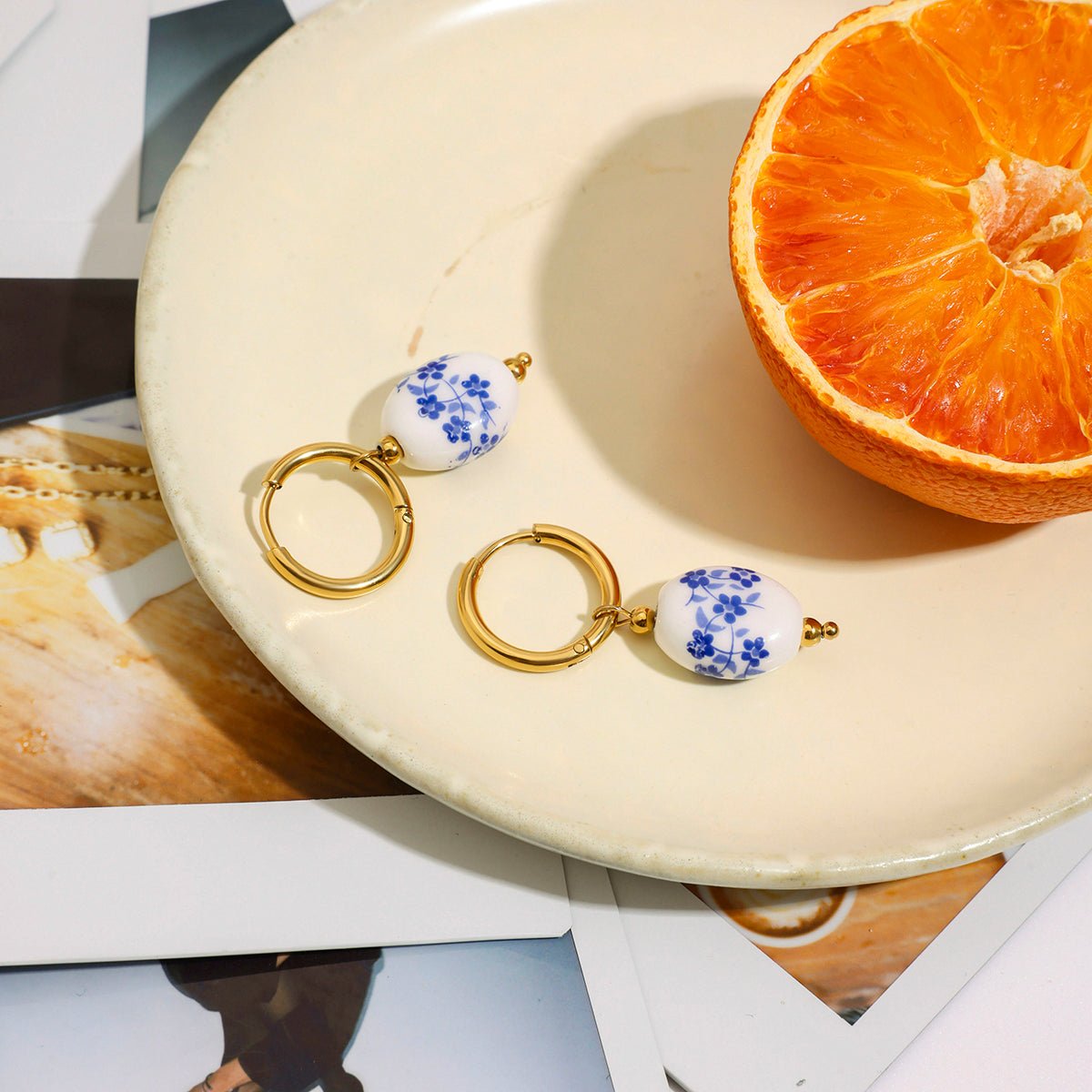 Pair of earrings with blue floral design on a white plate with an orange half.
