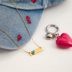 Gold necklace with heart pendant, denim jacket with red hearts, and pink heart keychain on a white surface