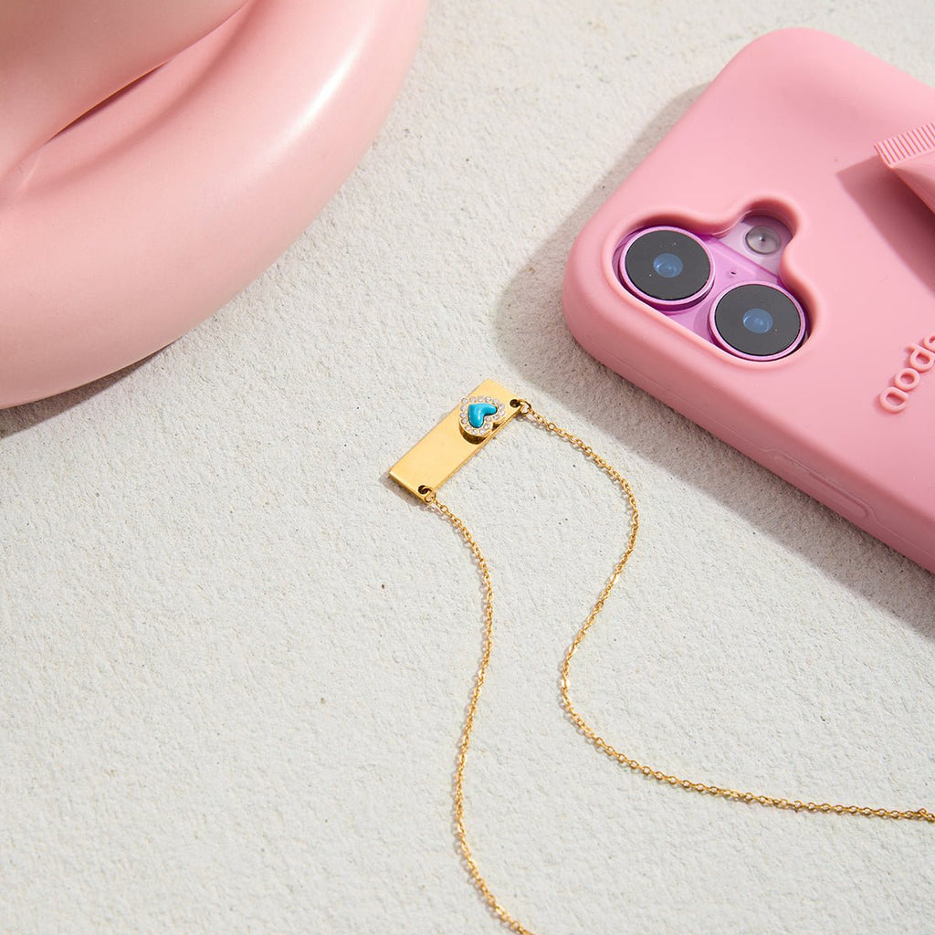 Gold necklace with a blue pendant on a pink phone case.