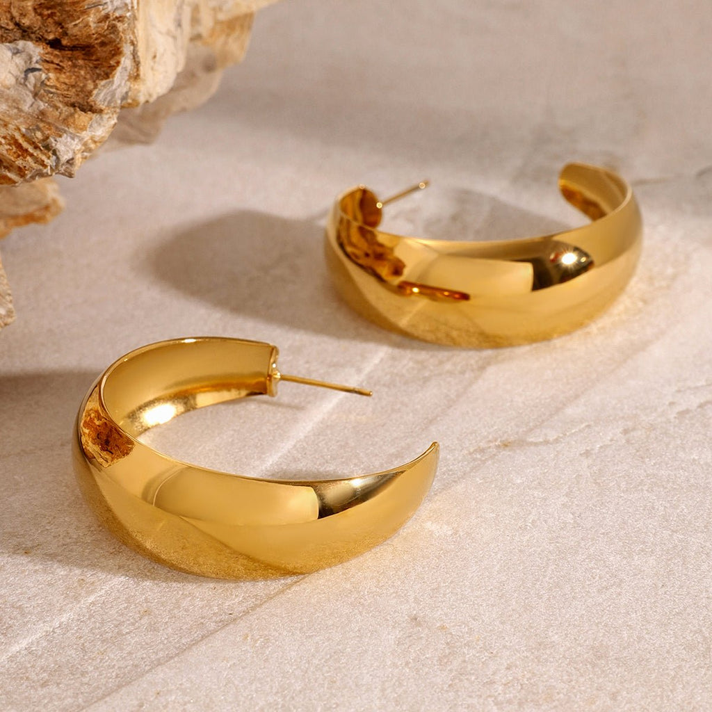 Gold hoop earrings on a textured beige surface with a natural rock background