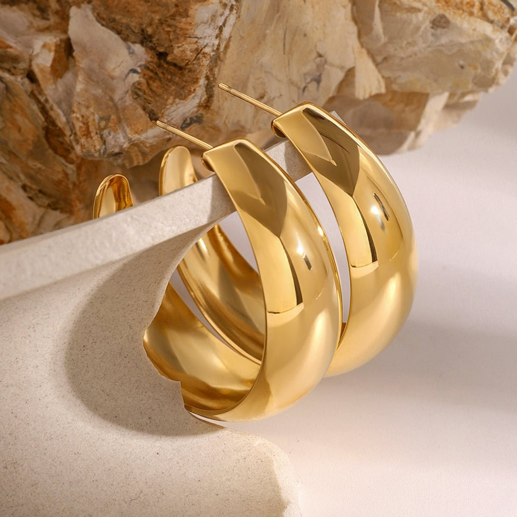 Gold hoop earrings on a textured surface with a stone background