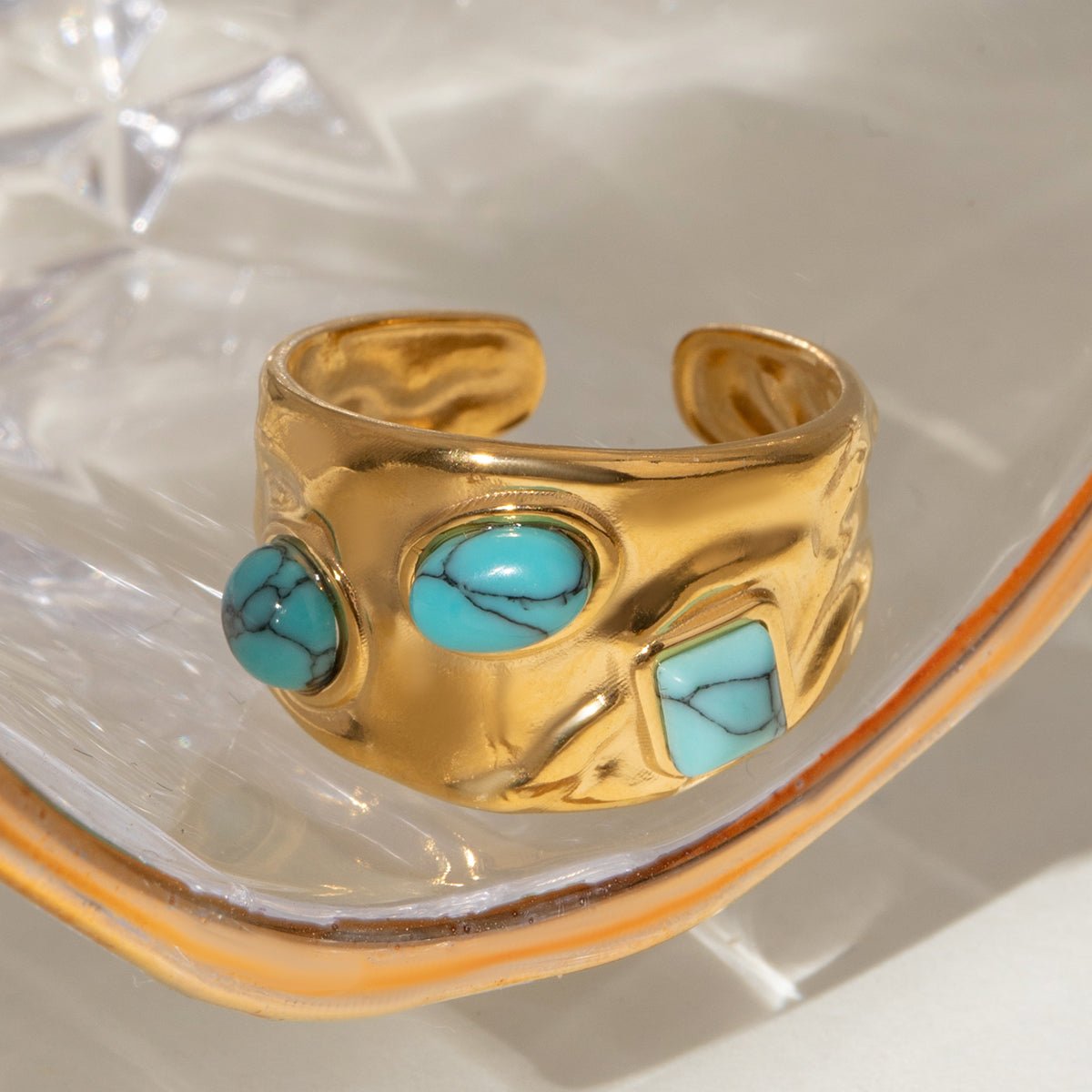 Gold ring with turquoise stones on a reflective surface