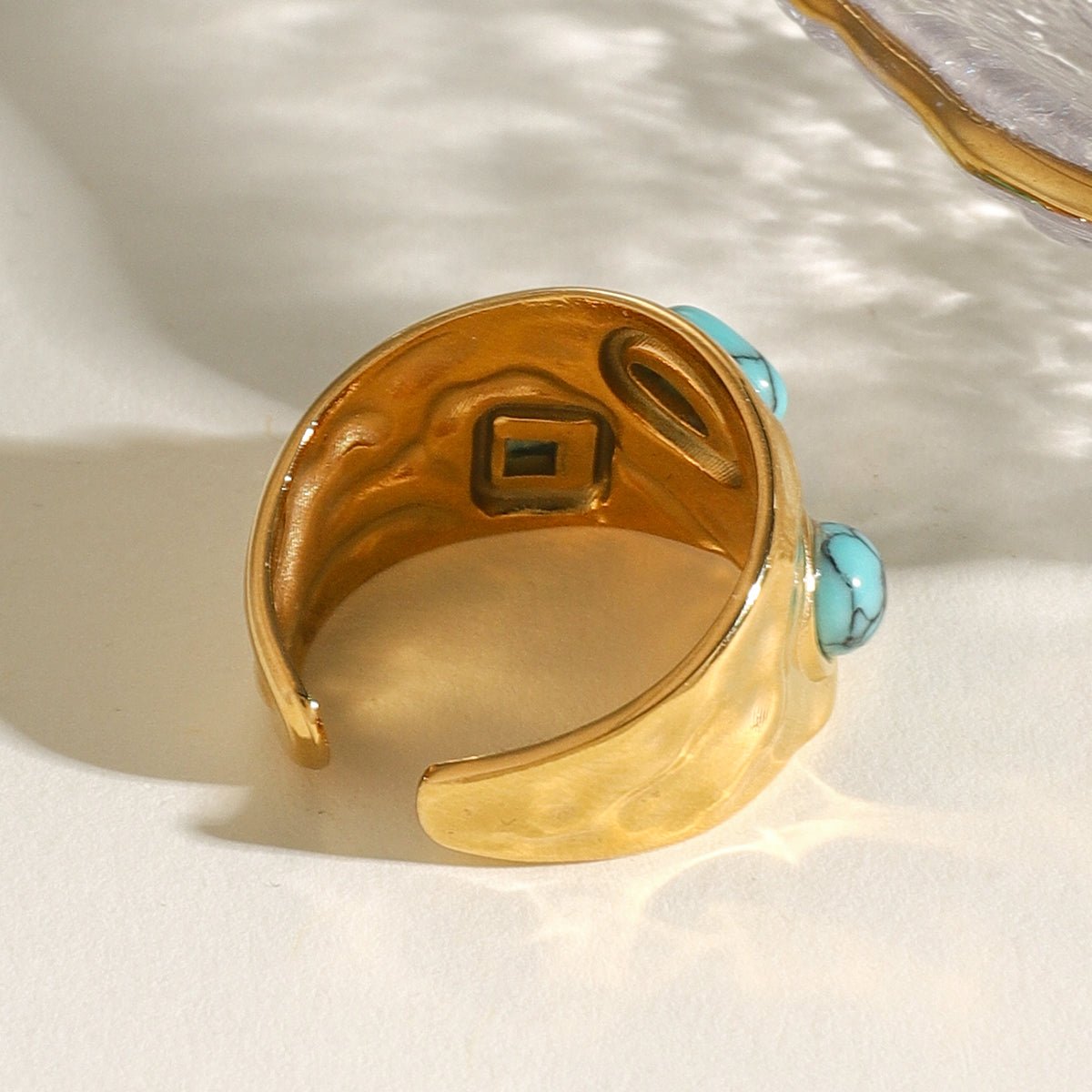 Gold ring with turquoise stones on a textured white surface