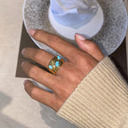 Gold ring with turquoise stones on a person's finger, blurred background