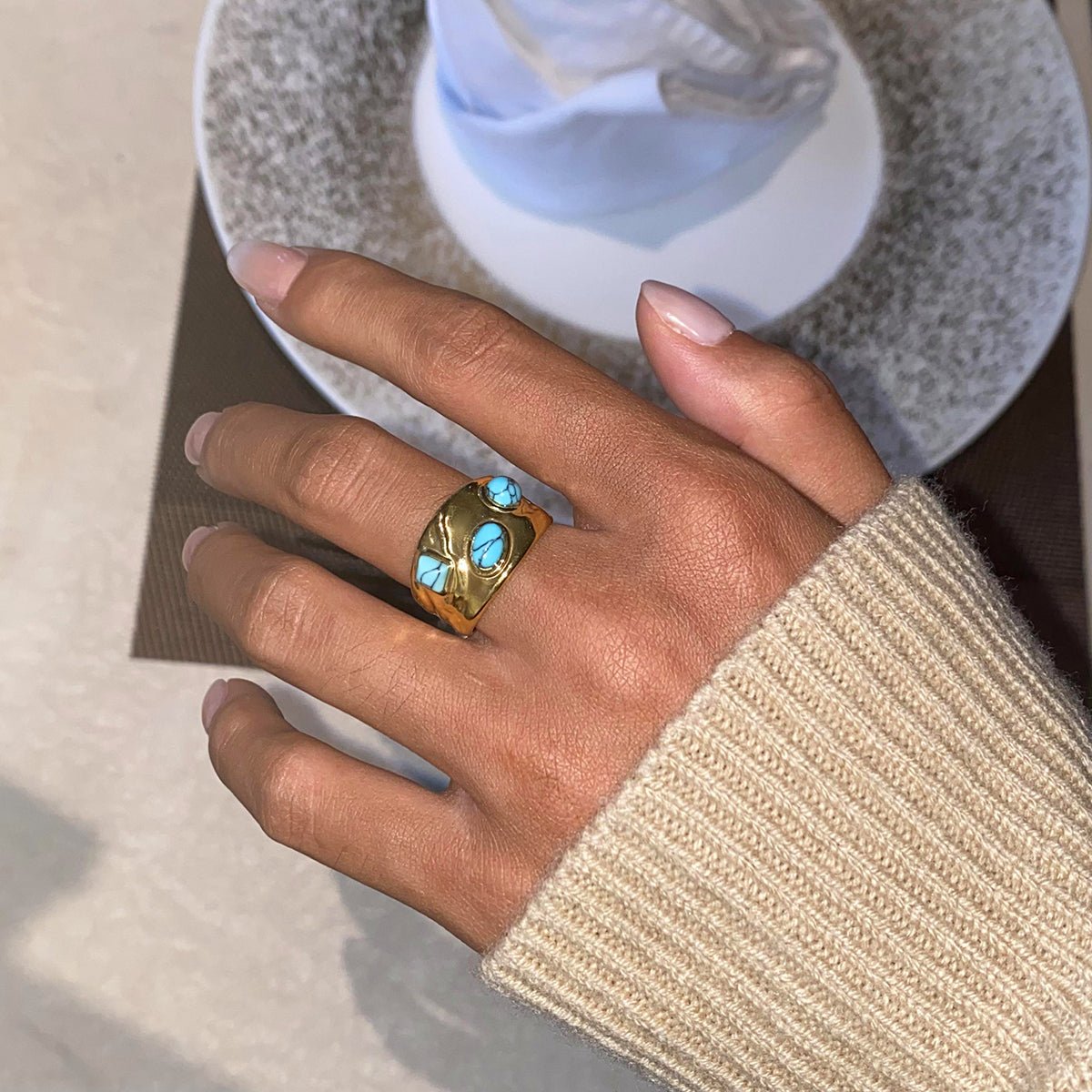 Gold ring with turquoise stones on a person's finger, blurred background