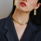 Woman wearing a gold necklace and earrings with a dark blazer.