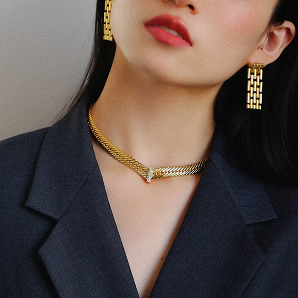 Woman wearing a gold necklace and earrings with a dark blazer.
