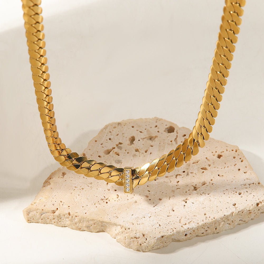 Gold chain necklace with a diamond pendant on a textured stone surface