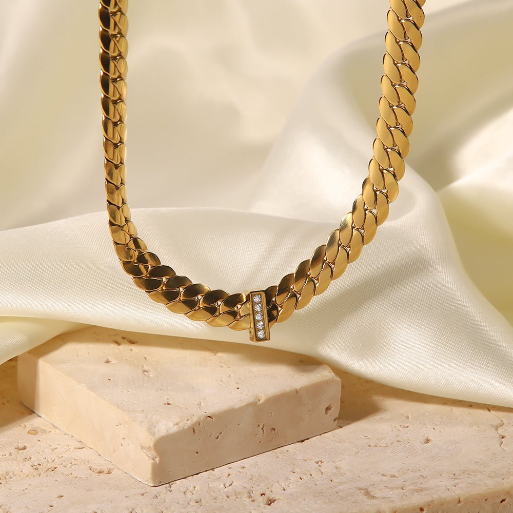 Gold chain necklace with diamond accents on a beige fabric background