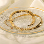 Gold chain necklace on a clear glass plate with a white fabric background