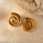 Gold spiral earrings on a textured beige surface