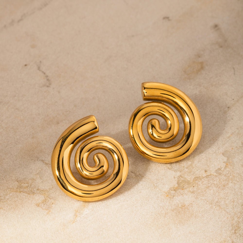 Pair of gold spiral earrings on a beige marble background