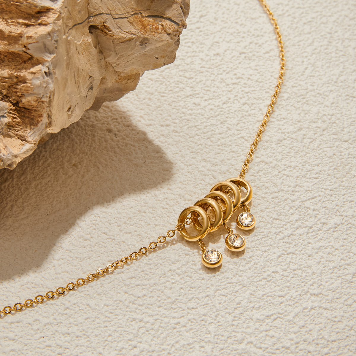 Gold necklace with circular pendants on a textured beige surface