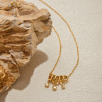 Gold necklace with pendant on a textured beige surface