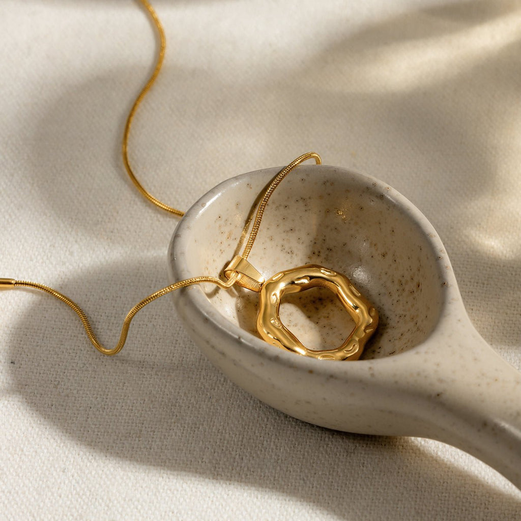 Gold necklace with a unique pendant in a small ceramic dish on a beige fabric background