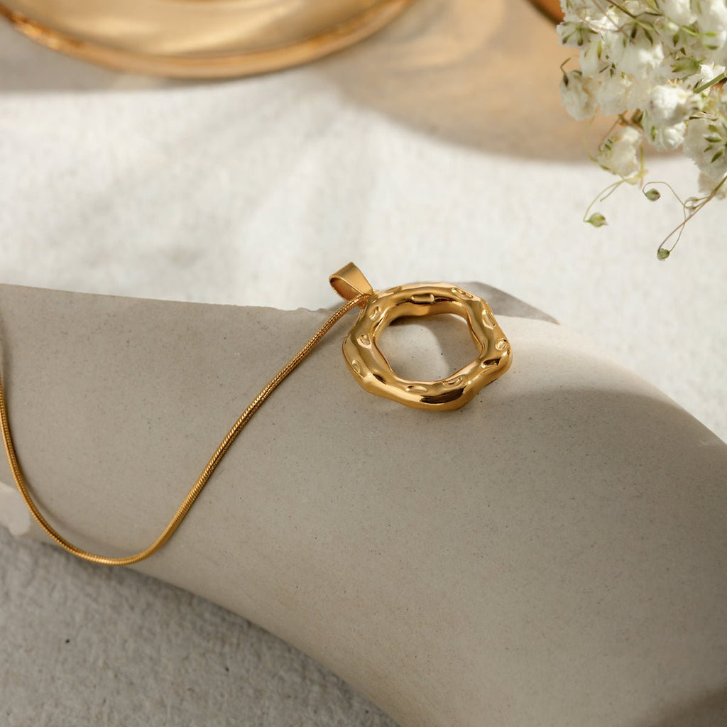 Gold necklace with a unique pendant on a light surface with flowers in the background