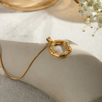 Gold necklace with a unique pendant on a light surface with flowers in the background