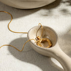 Gold necklace with a pendant in a ceramic dish on a textured surface