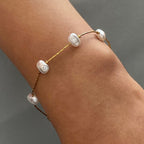 Gold bracelet with pearls on a wrist against a gray background