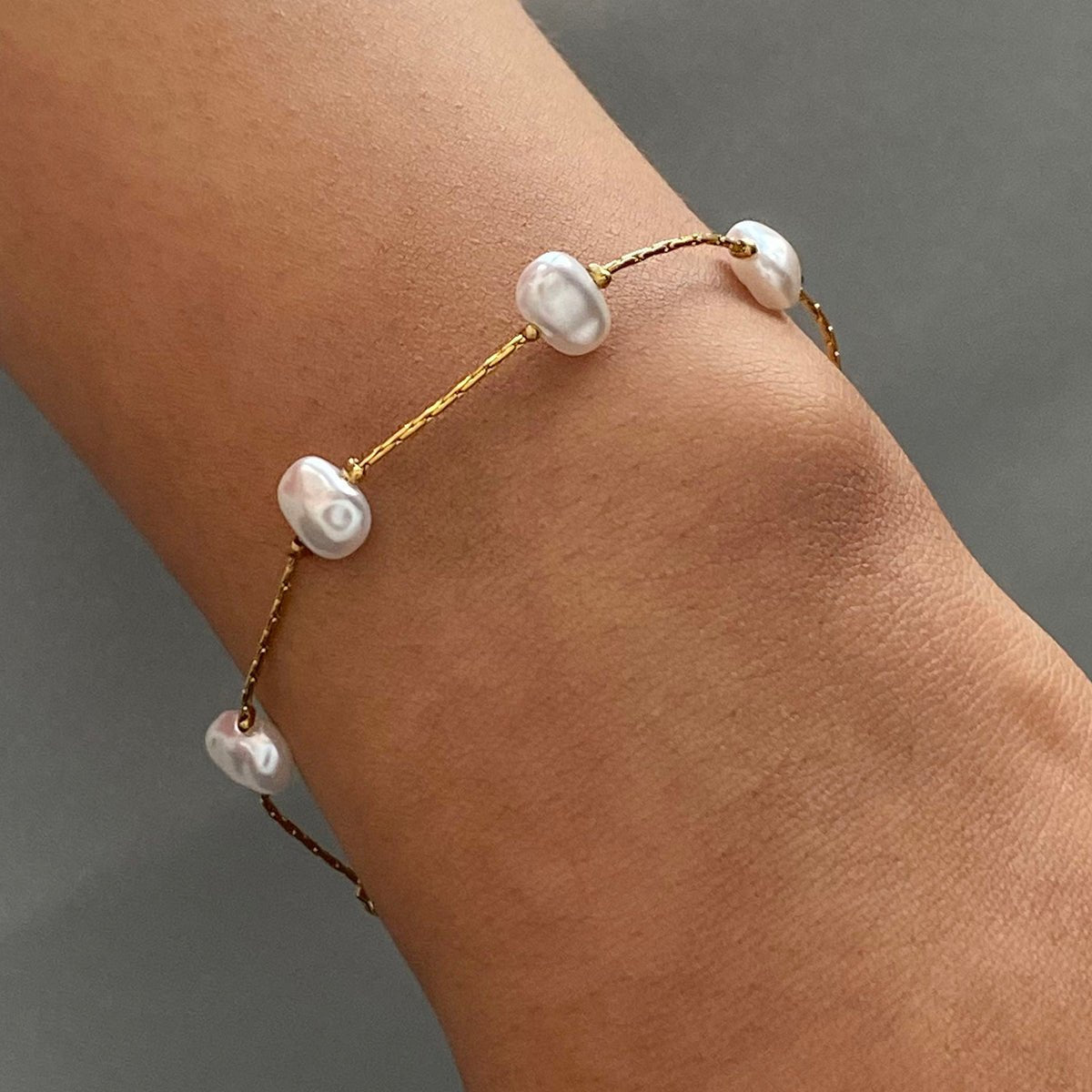 Gold bracelet with pearls on a wrist against a gray background