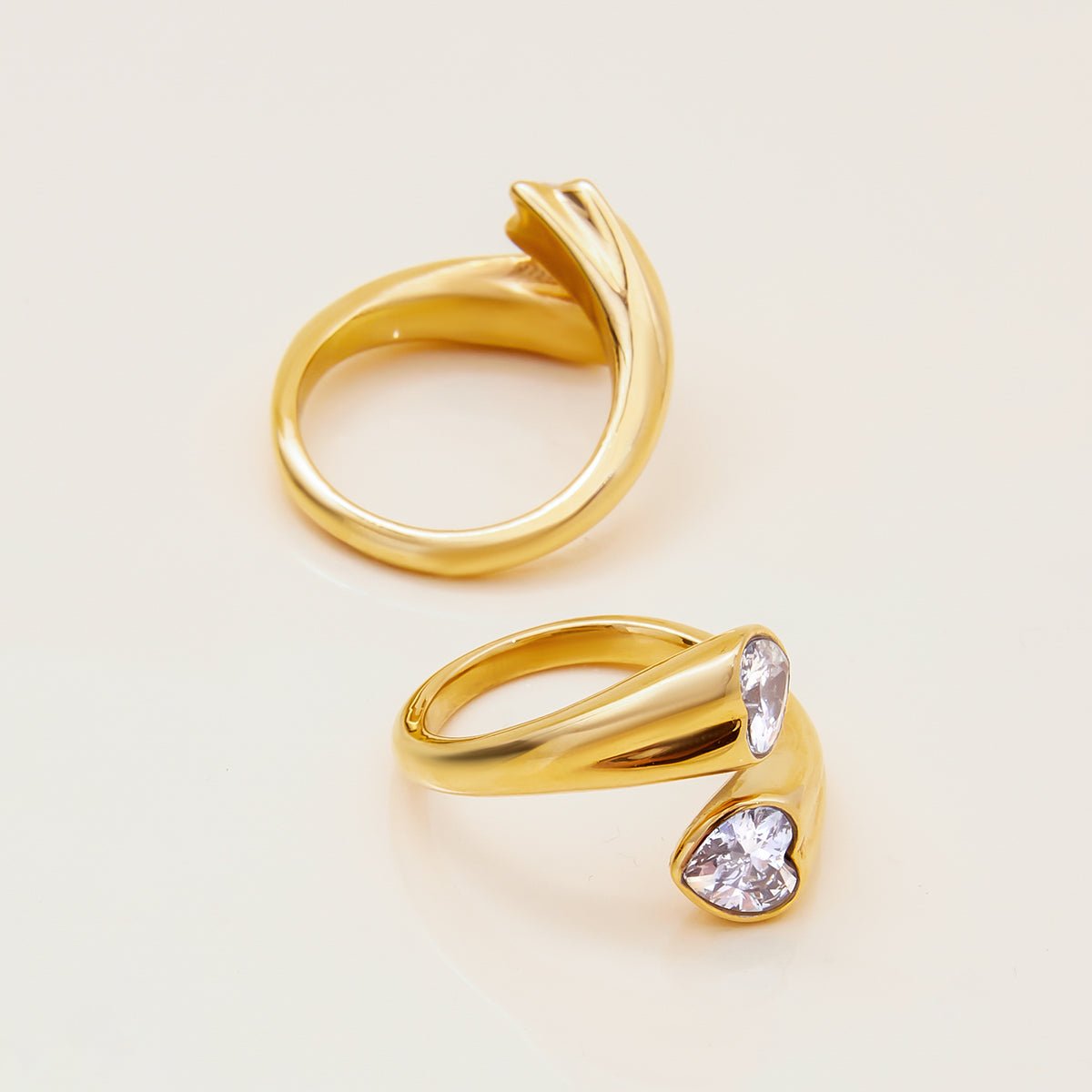 Two gold rings with heart-shaped gemstones on a light beige background