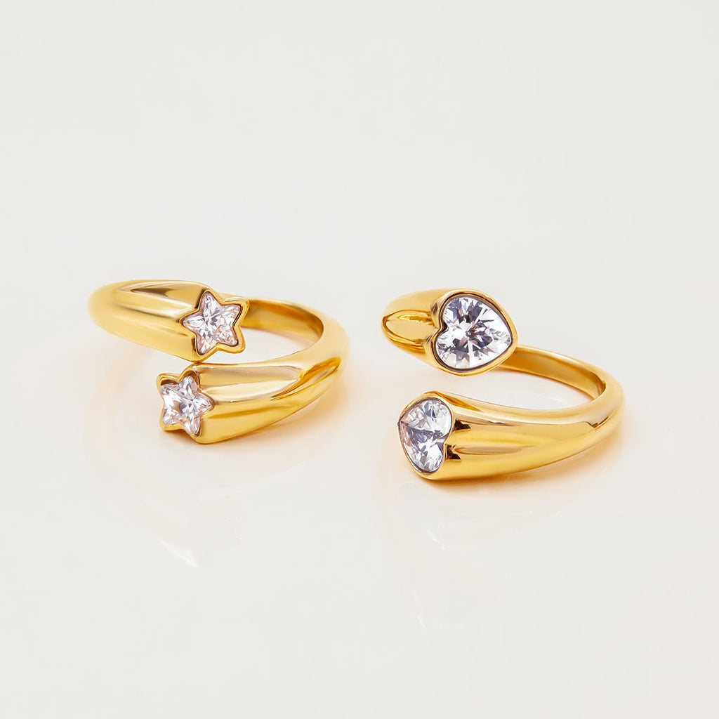Two gold rings with star and heart-shaped gemstones on a light beige background