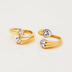 Two gold rings with star and heart-shaped gemstones on a light beige background