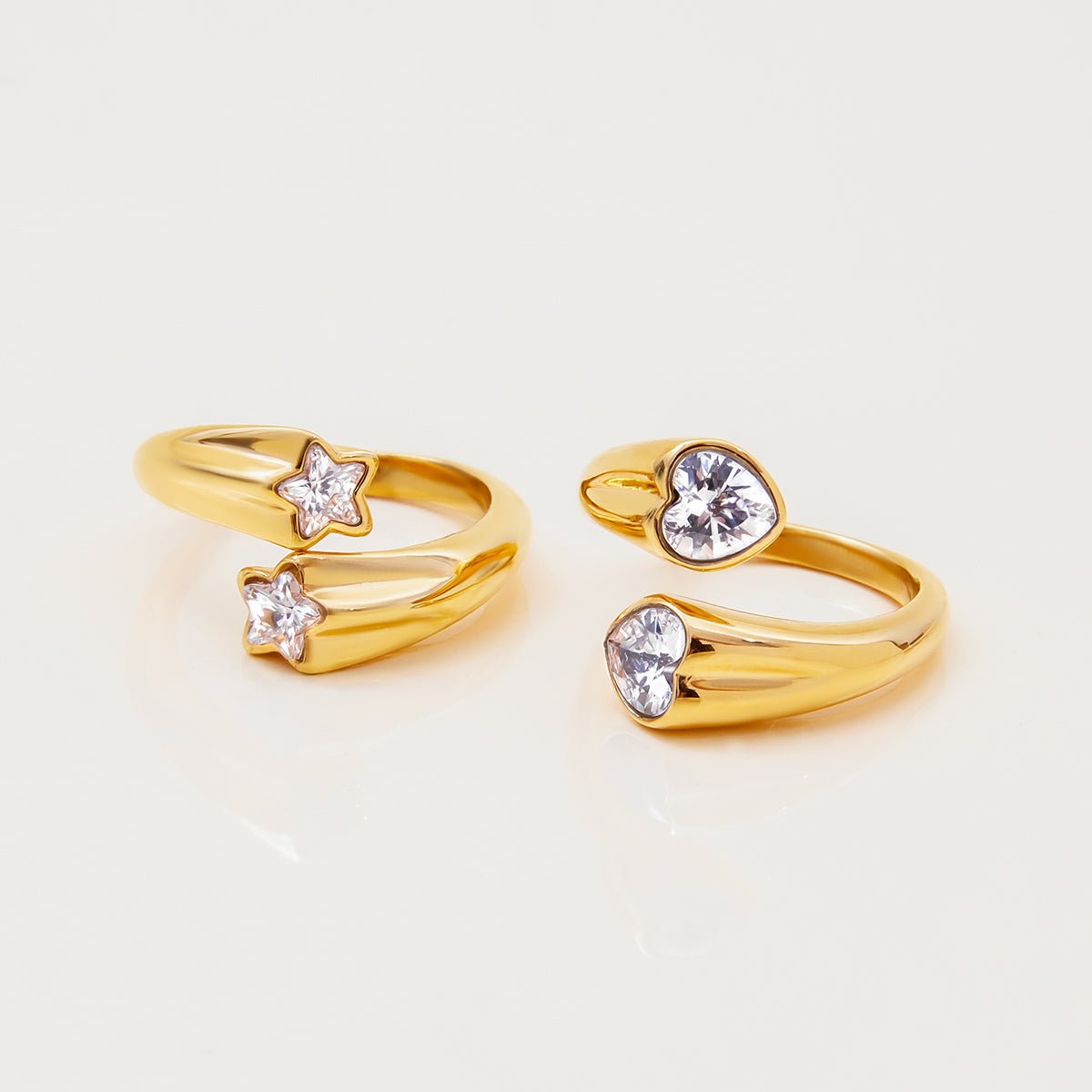 Two gold rings with star and heart-shaped gemstones on a light beige background