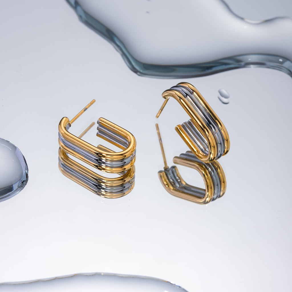 Gold and silver hoop earrings on a reflective water surface