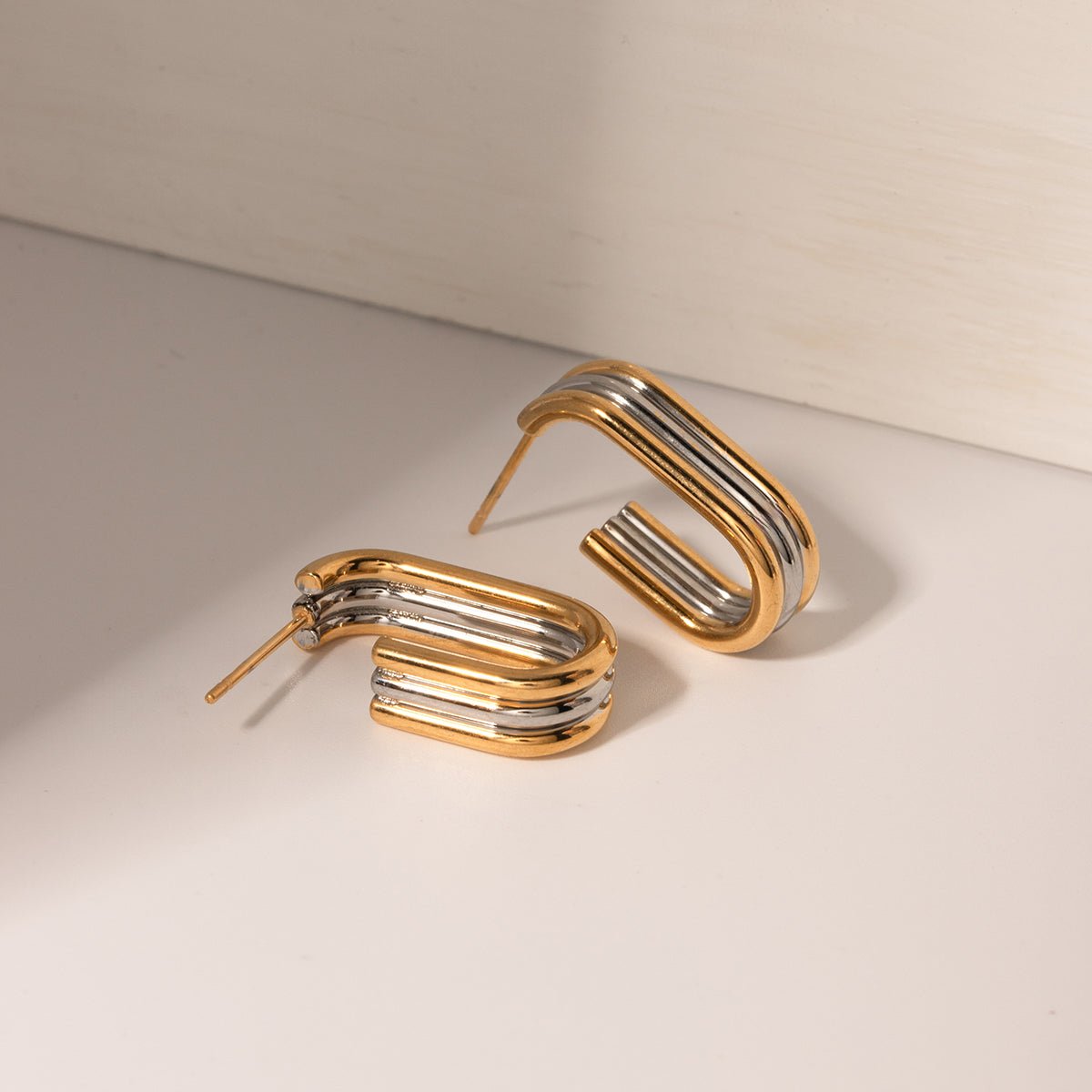 Pair of gold and silver hoop earrings on a beige background