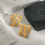 Gold and silver earrings on a white surface with a black box and white packaging in the background.