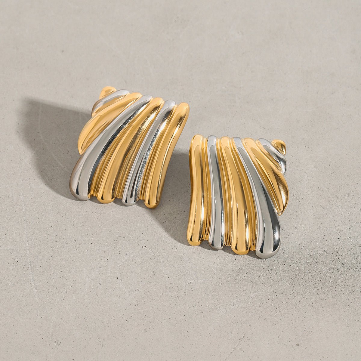 Pair of gold and silver earrings on a beige background