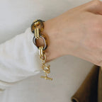 Gold bracelet with a lion head charm on a wrist against a neutral background
