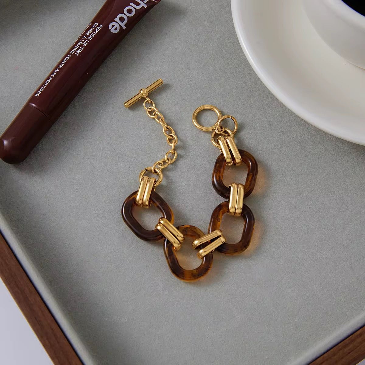 Gold and tortoiseshell chain bracelet on a gray surface with a pen and white dish in the background.