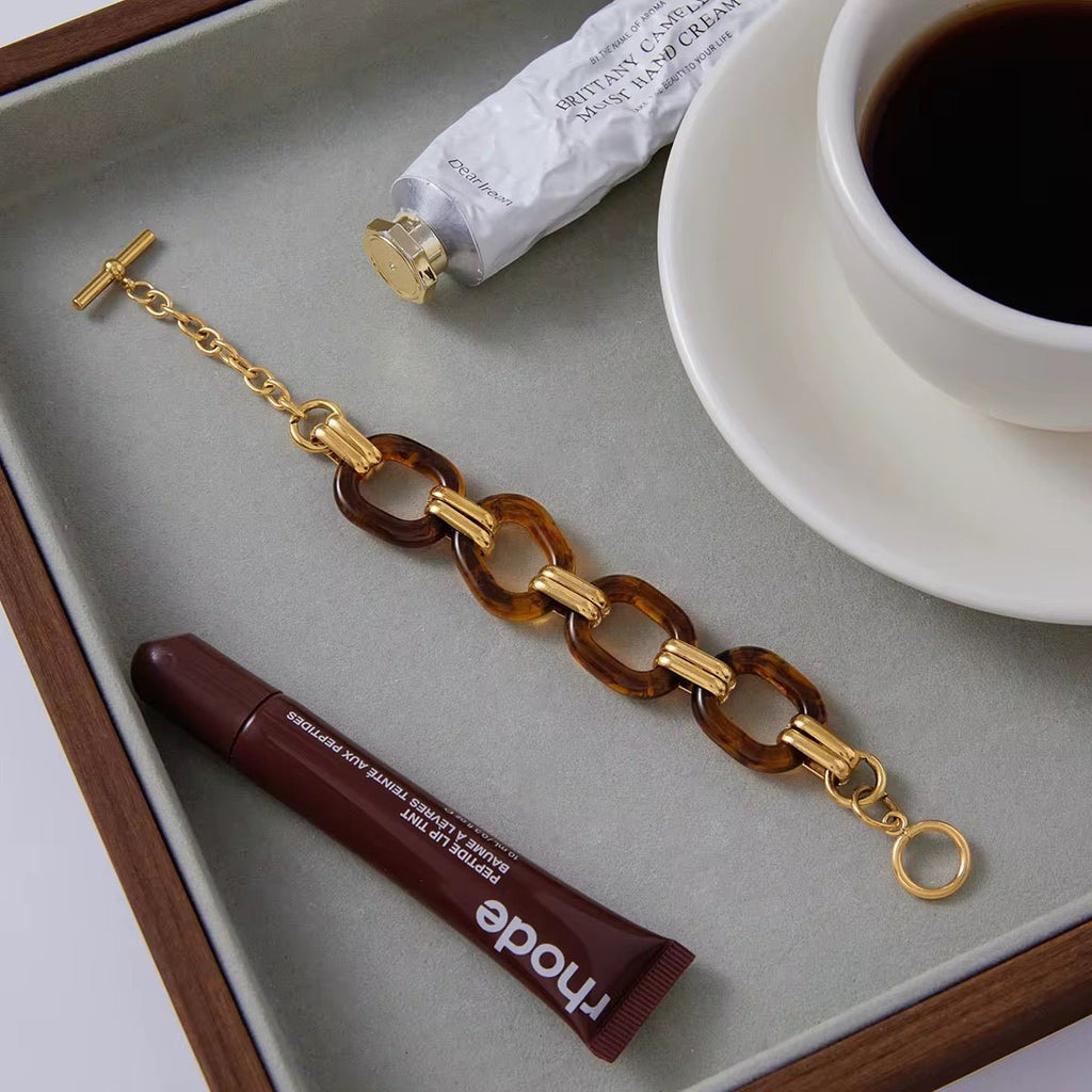Bracelet with tortoiseshell and gold links on a tray with coffee and skincare products.