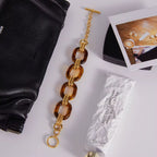 Gold and tortoiseshell chain bracelet on a white surface with a black pouch and cream tube.