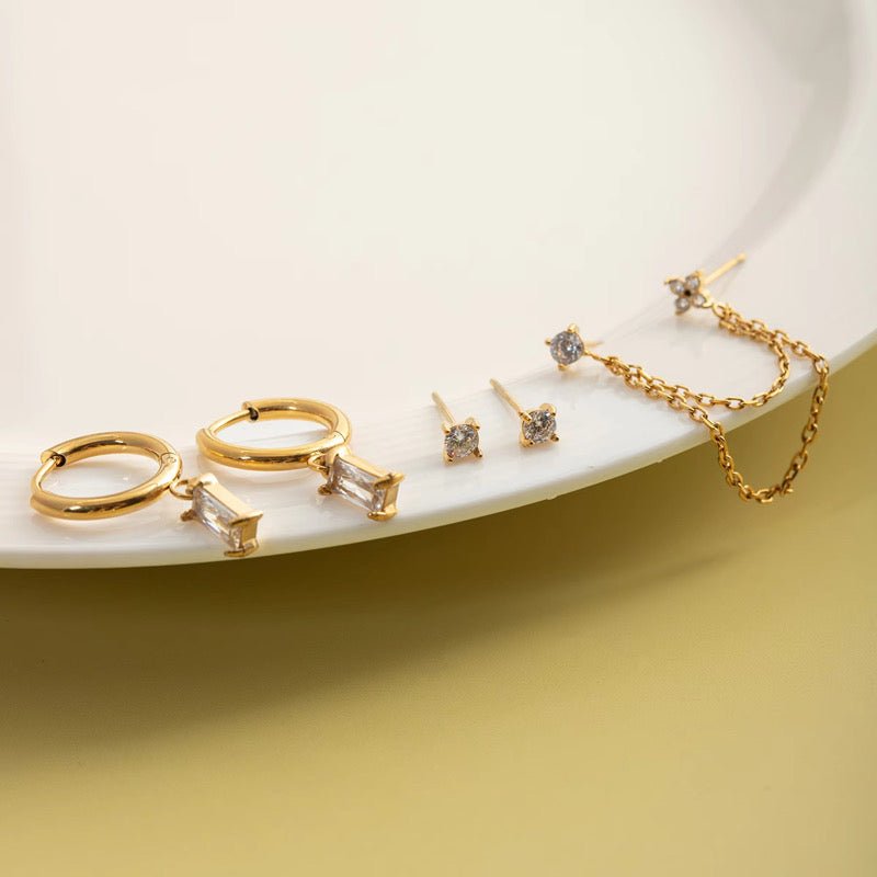 Set of gold earrings on a white plate with a yellow background