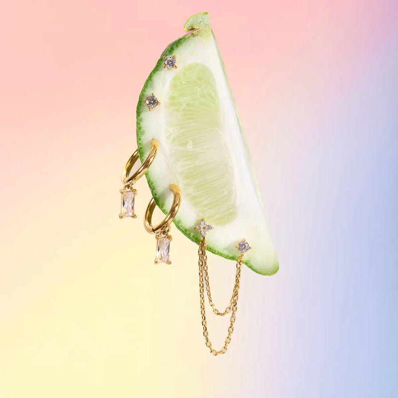 Gold jewelry with gemstones on a sliced lime against a gradient background