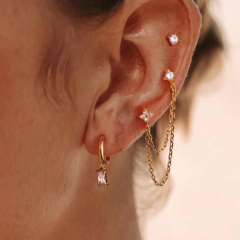 Close-up of an ear wearing gold earrings with gemstones on a blurred background